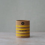 Cylindrical container of sea salt rub with striped design on a gray background