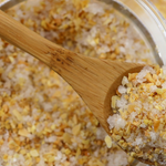Wooden spoon filled with a mixture of yellow and white granules, possibly salt and flowers, over a container.