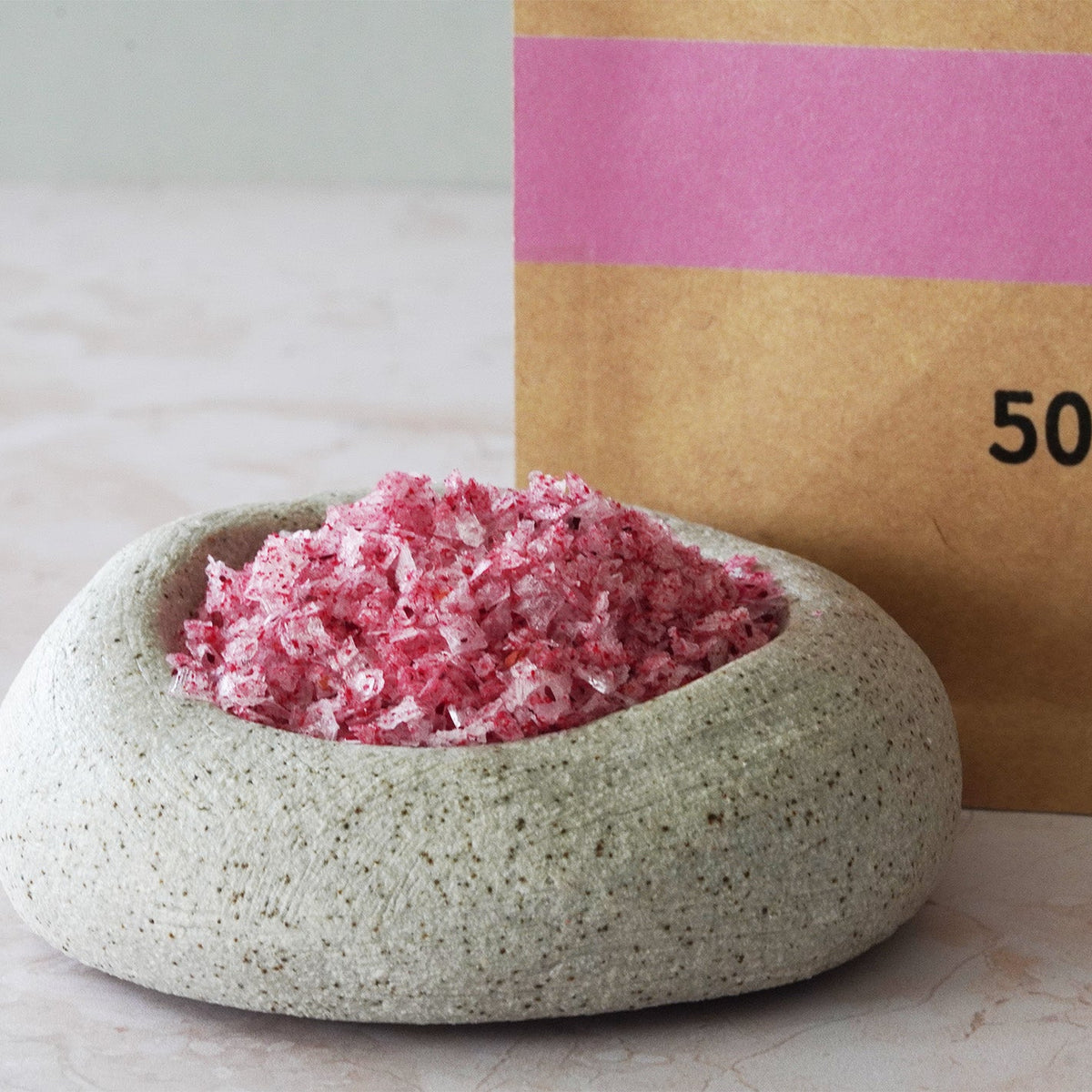 Pink granulated product in a stone container with a brown box labeled '500g' in the background.