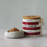 Container of Olsson's Red Gum Smoked Salt with a wooden lid on a light surface.
