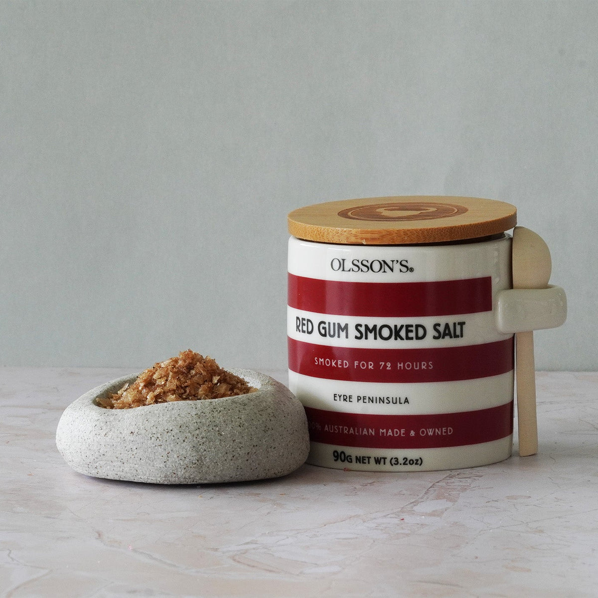 Container of Olsson's Red Gum Smoked Salt with a wooden lid on a light surface.