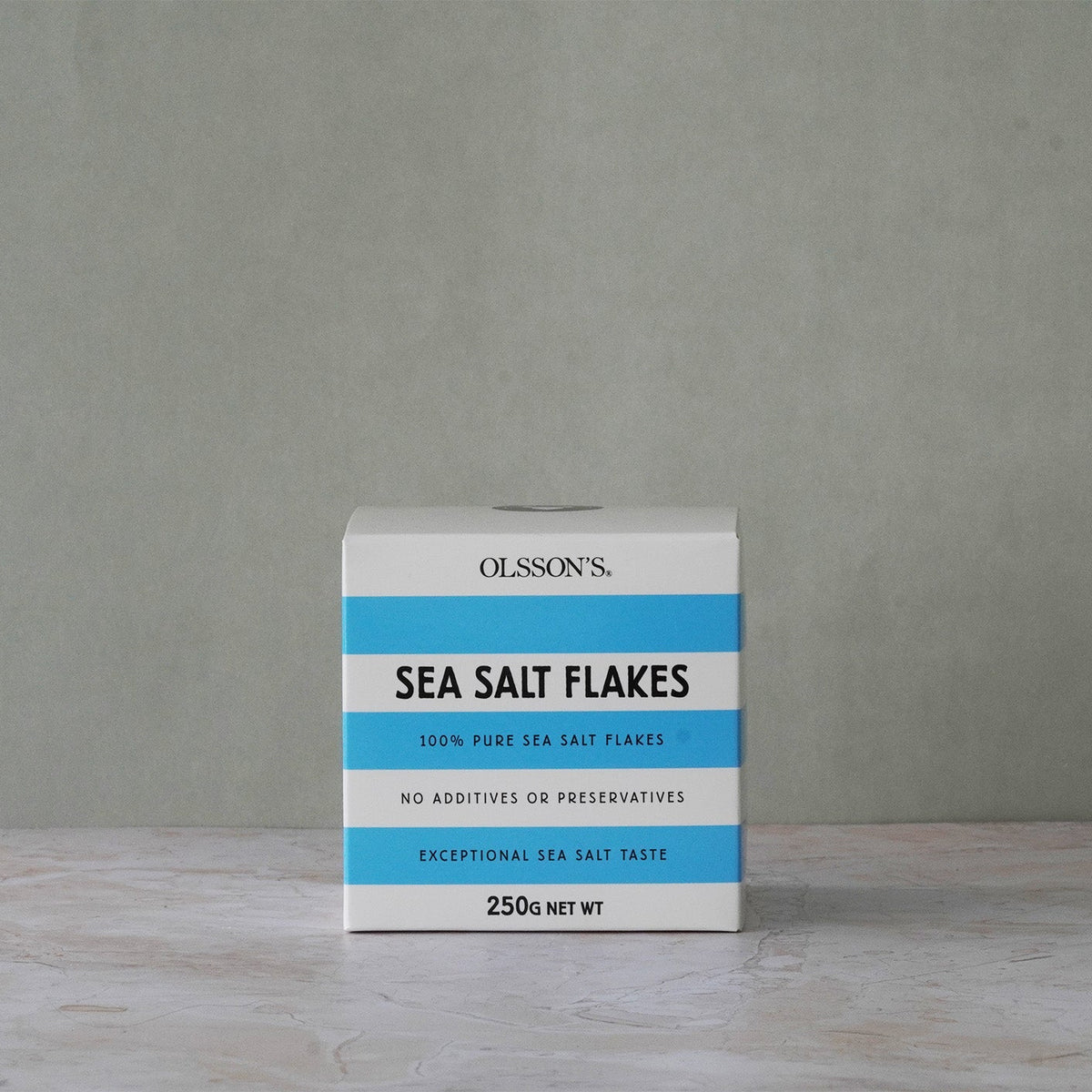 Box of Olsson's Sea Salt Flakes on a wooden surface with a gray background