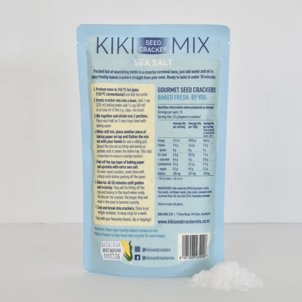 A light blue pouch of Kiki Seed Cracker Mix gourmet seed crackers, shown with a small pile of white cracker pieces in the foreground against a light gray background.