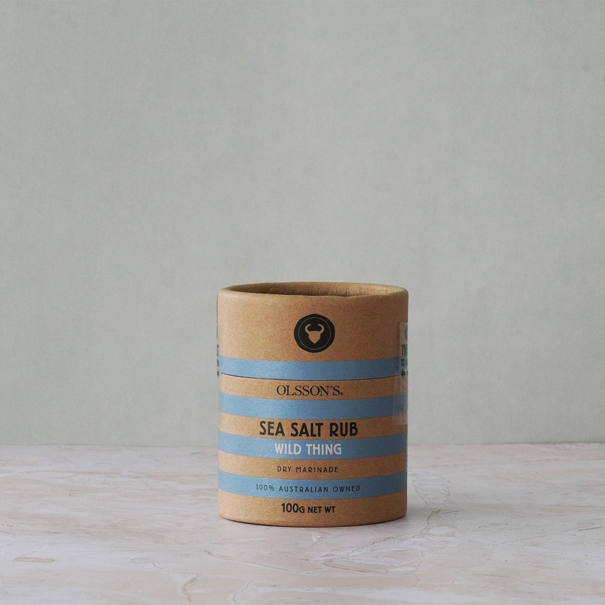 Cardboard container of Olsson's Sea Salt Rub on a wooden surface with a gray background